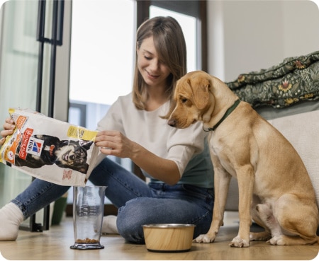 Kobieta wsypuje karmę firmy Hill's Pet Nutrition do miarki, podczas gdy pies przygląda się jej z uwagą.