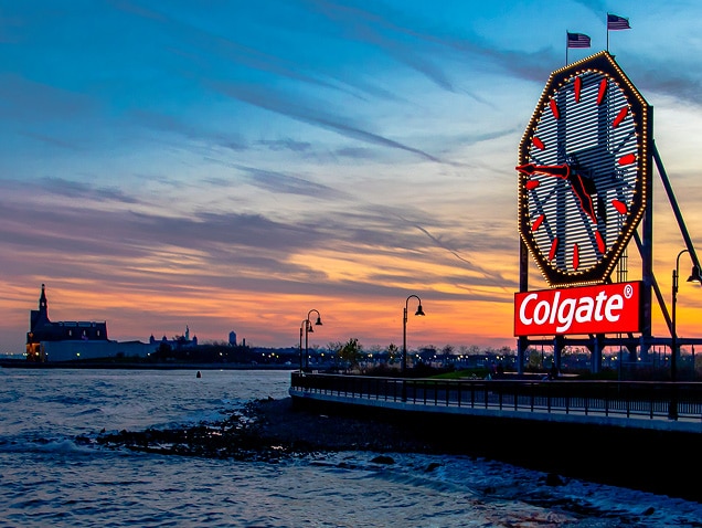brzeg morza, logo Colgate w tle pod dużym zegarem z czerwonymi wskazówkami